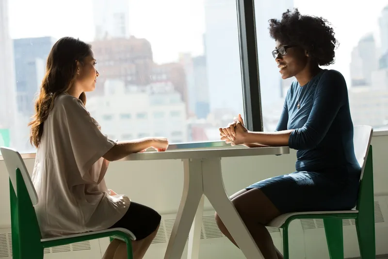 Two women in warm conversation at a table by a window