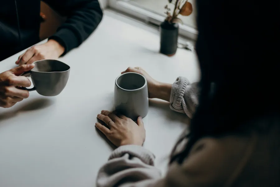 Two people sitting with warm mugs in a quiet conversation